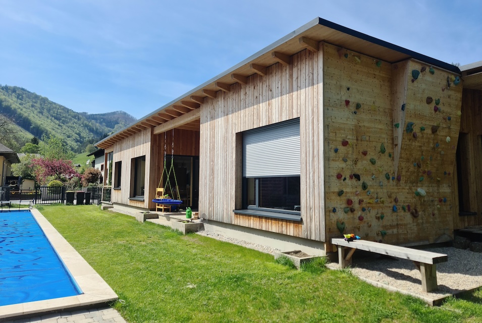 Garten des Einfamilienhauses mit Schwimmbecken, Schaukel und Kletterwand an der Holzfassade des Hauses